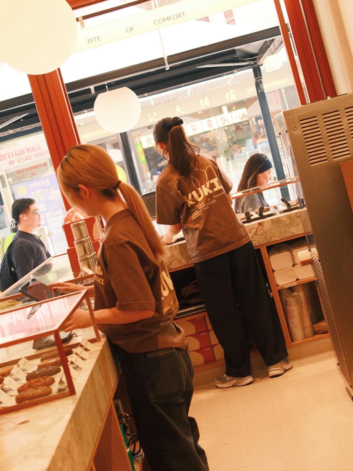 KUKI staff in brown tees working the Burwood counter, with the street visible through the windows.