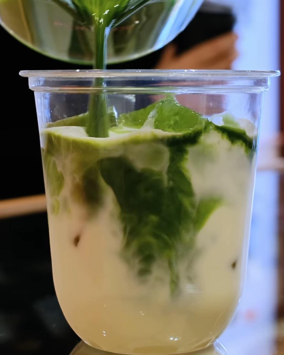 Bright green matcha poured from a glass jug into an iced drink at KUKI.