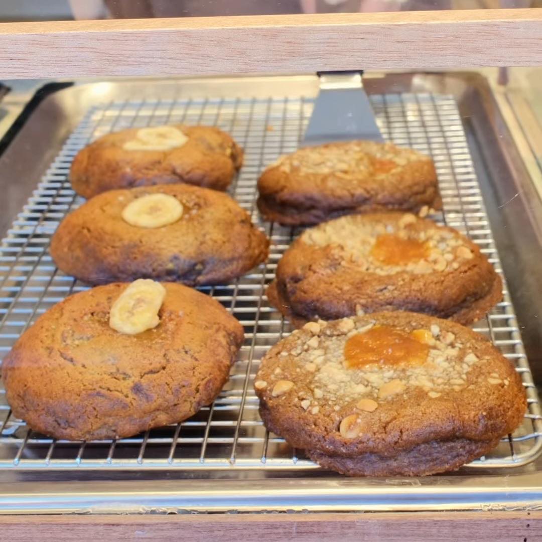 Cookies topped with banana slices and with crushed hazelnut and toffee, cooling on a wire rack at KUKI.